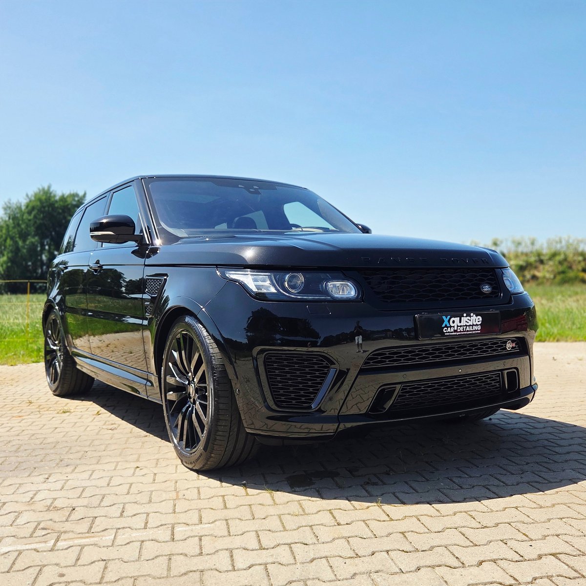 Black Range Rover sport vehicle parked on brick paving with green landscape in background